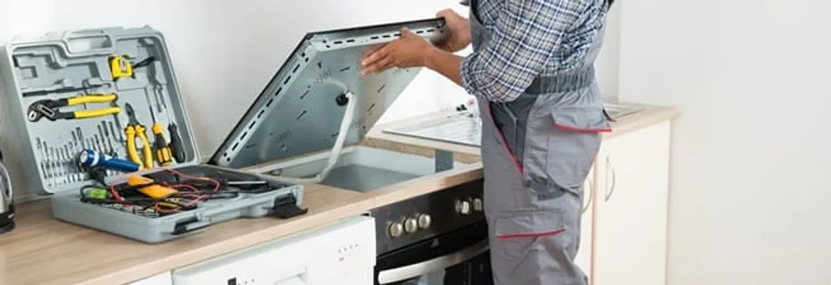 Cooktop repair technician lifting a built-in stovetop for service in Wichita, KS