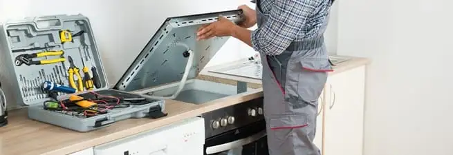 Cooktop repair technician lifting a built-in stovetop for service in Wichita, KS