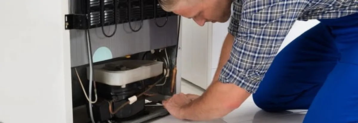 Refrigerator repair technician servicing the compressor and condenser area in Wichita, KS