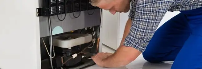 Refrigerator repair technician servicing the compressor and condenser area in Wichita, KS