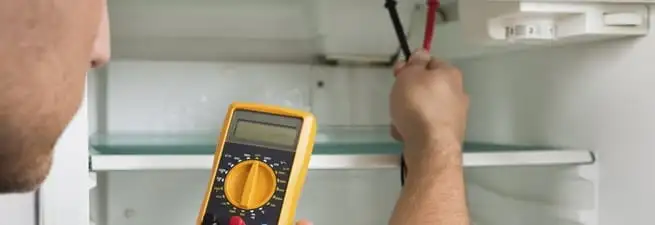 Refrigerator repair technician testing electrical components with a multimeter in Wichita, KS