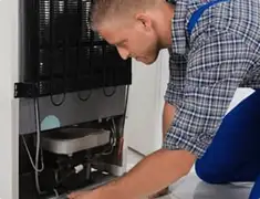 Refrigerator repair technician servicing the compressor and condenser area in Wichita, KS