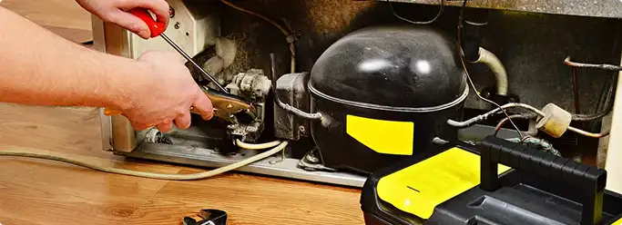 Refrigerator repair technician fixing the compressor and wiring in Wichita, KS